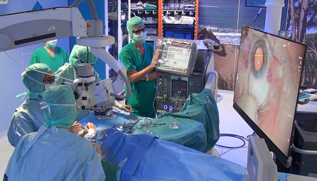 An image of a group of surgeons in an operating room with a patient undergoing surgery. An NGENUITY screen shows a close-up view of the surgery to the surgeons in the room.