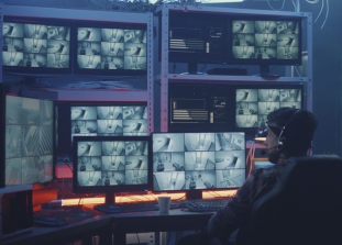 An image of a man sitting in a chair with many computer screens in front of him