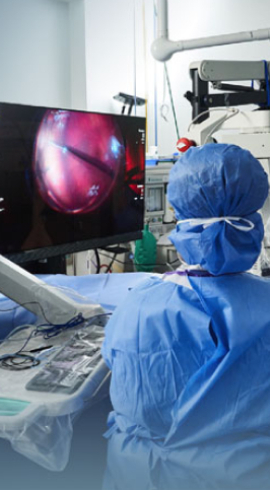 An image of a surgeon wearing blue scrubs in the operating room, observing a surgical operation on a screen.