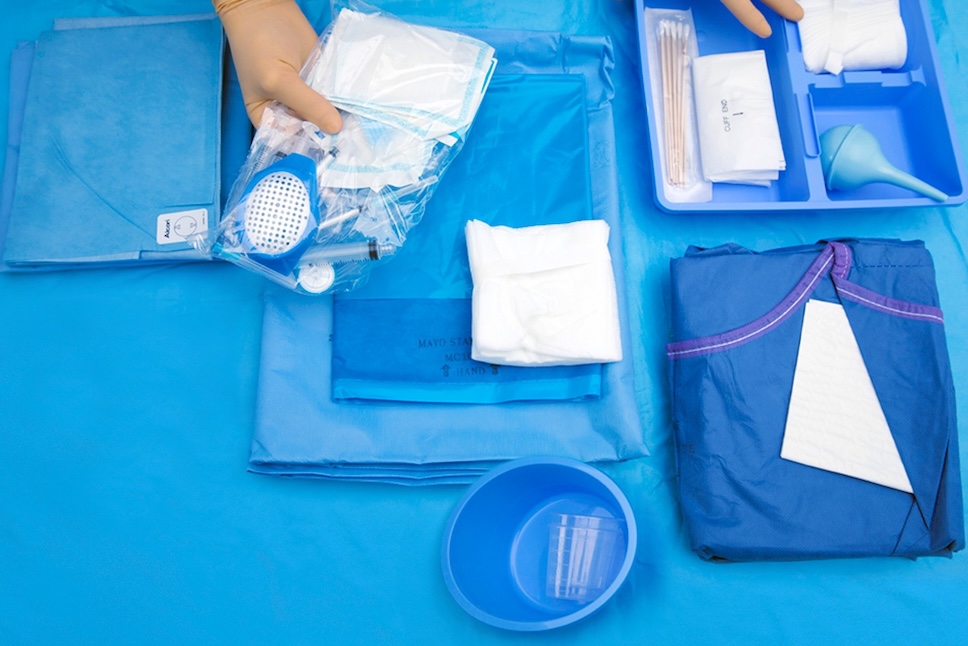 Hand holding a sterile surgical pack containing Alcon instruments and supplies, placed on a blue surgical drape