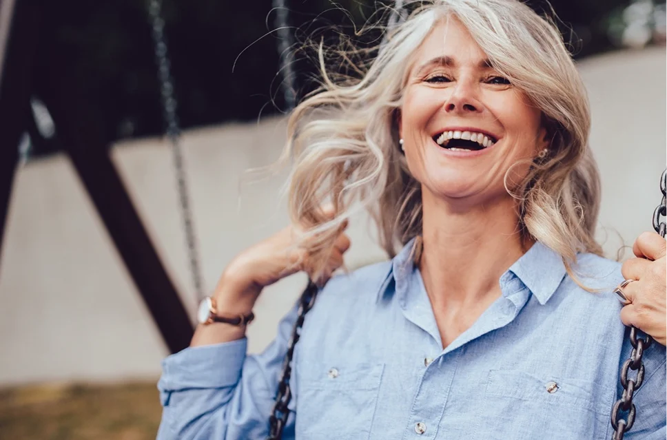 A smiling older woman sitting outdoors, symbolizing high patient satisfaction and freedom from glasses.